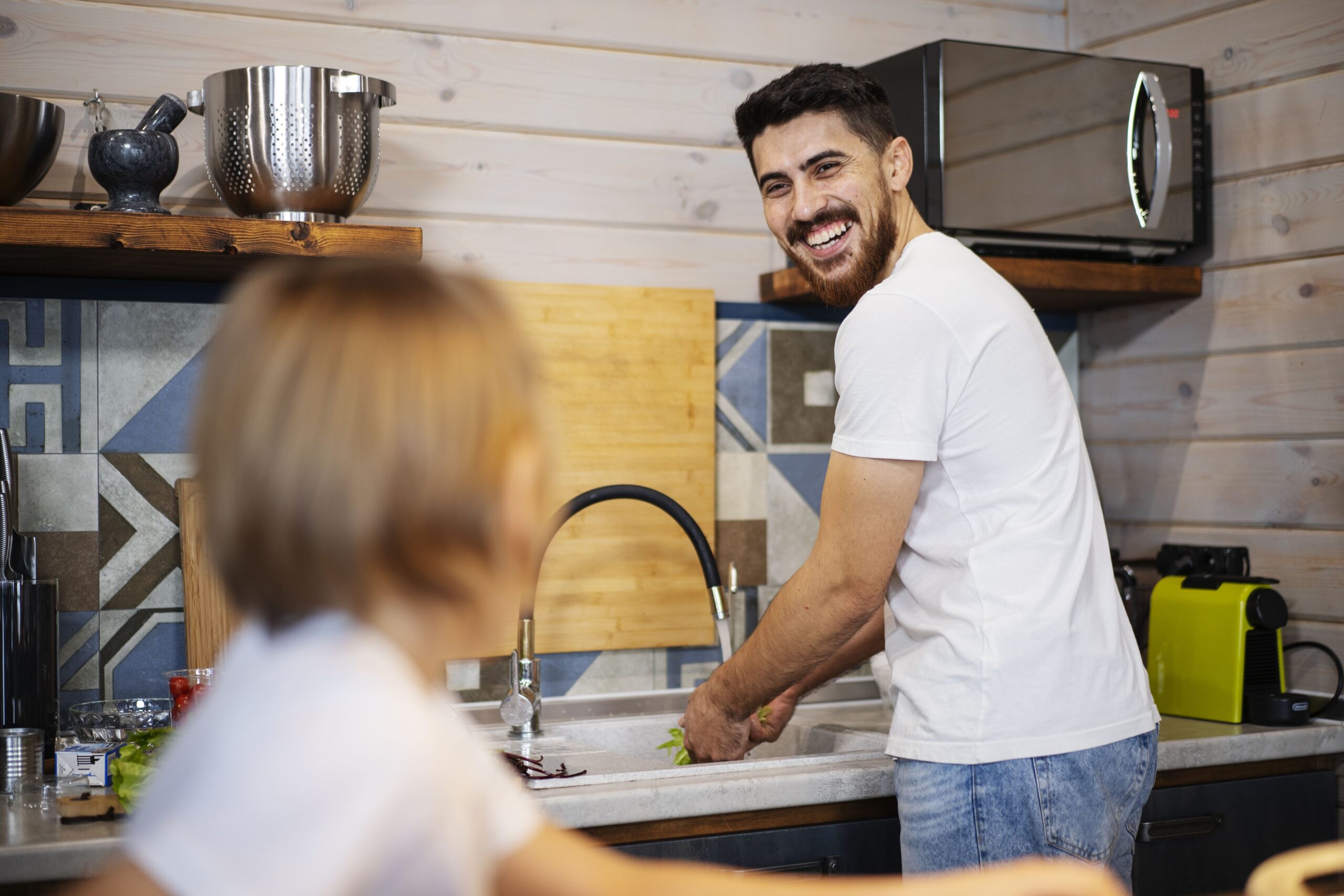 A father in Lake County, FL, is smiling at his child while washing vegetables in a kitchen sink, highlighting the use of clean, purified water for food preparation.