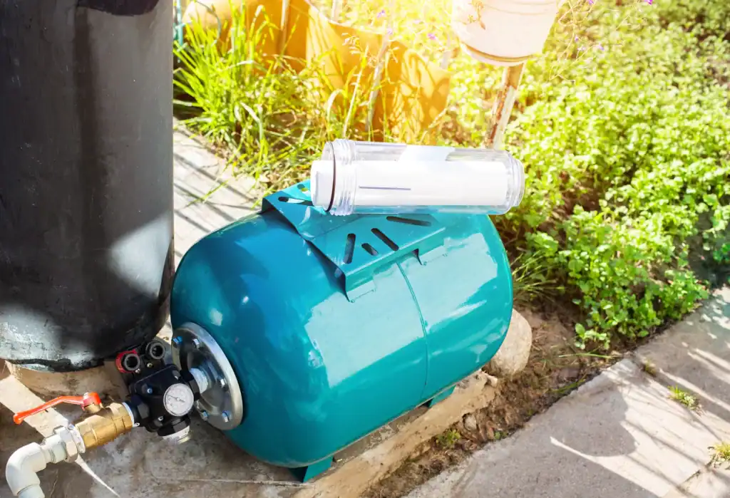 A blue water pressure tank with a transparent filter housing and pressure gauge is set up outdoors in Lake County, FL, surrounded by greenery and sunlight.