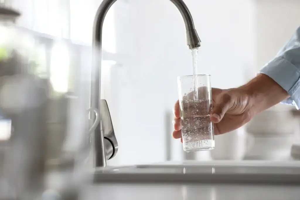 A close-up of a hand filling a clear glass with water from a running faucet in a kitchen setting in Lake County, FL.