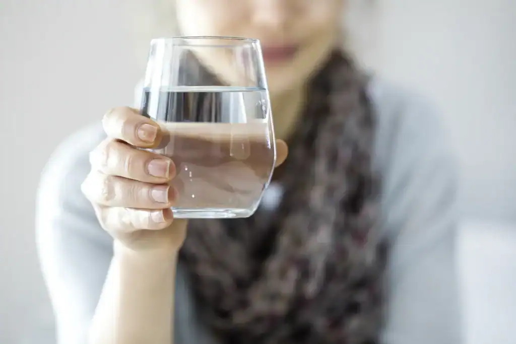 A person in Lake County, FL holds a clear glass of water in the foreground, with their hand prominently visible and the background softly blurred.