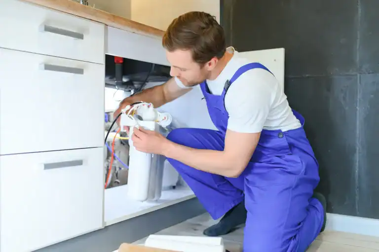 A professional plumber in Lake County, FL, is kneeling and working on a water filtration system installed under a kitchen sink.