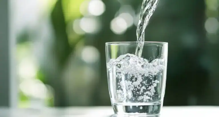 Water is poured into a clear glass, forming bubbles as it fills, with a blurred green and white outdoor background in Lake County, FL.