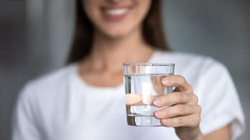 A person in a white shirt holds a clear glass of water in their right hand, smiling in a blurred background—capturing a moment of clean water appreciation in Lake County, FL.