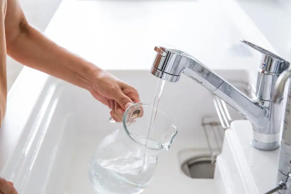 A person fills a clear glass pitcher with water from a modern kitchen faucet over a white sink, showcasing the benefits of Water Filtration Systems in Lake County, FL.