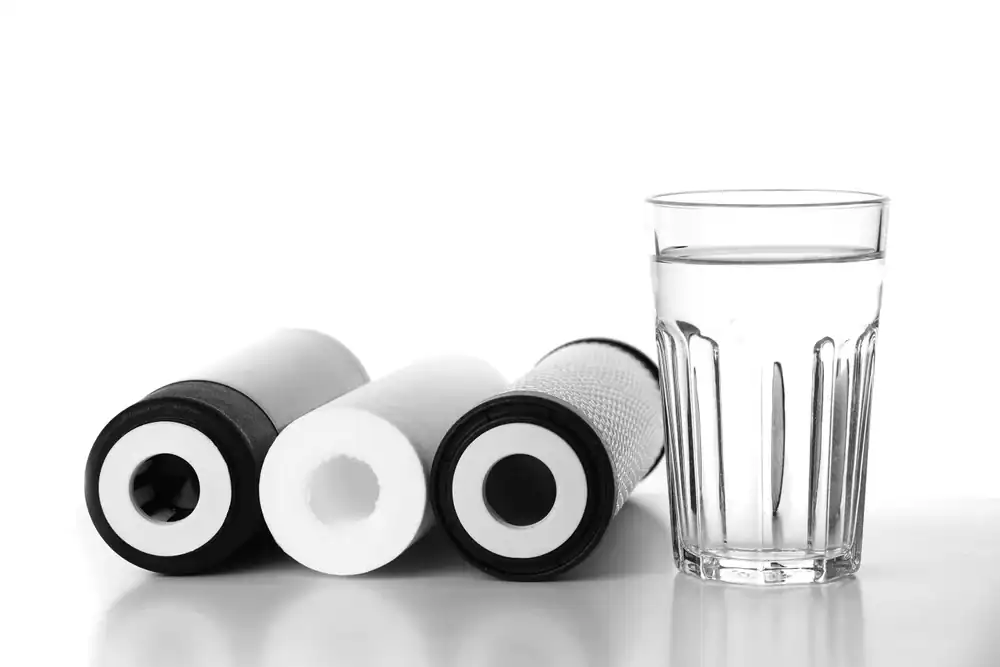 Three cylindrical water filters from top Water Filtration Systems Lake County, FL, are lying next to a clear glass filled with water, all set against a white background.